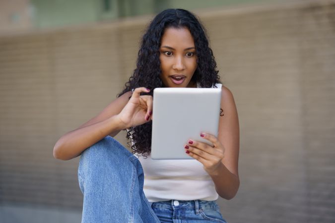 A young woman, full of excitement, is happily engaged with her tablet device while outdoors