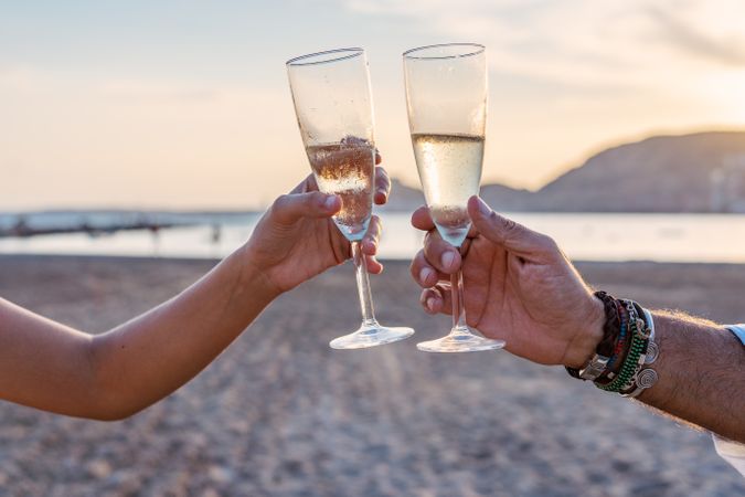 Crop women clinking wineglasses on beach during sunset