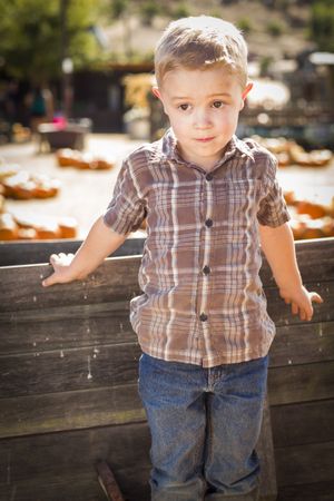 Little Boy Standing Against Old Wood Wagon at Pumpkin Patch.