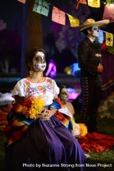 Woman sitting at altar for Day of the Dead wearing traditional makeup and dress bDGlp4