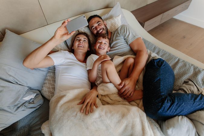 Family lying on bed and taking selfie at home