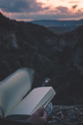 View to small river in canyon and legs of person with book sitting on the edge