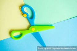 Open blue & green children's scissors on paper background bxA7Yn