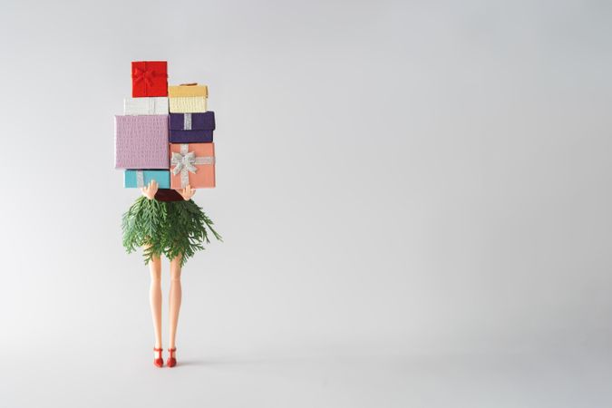 Barbie like doll with skirt made out of green winter branches holding stack of presents