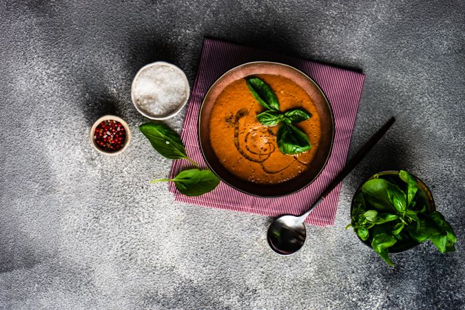 Top view of tomato soup with oil garnish and herbs, peppers and salt
