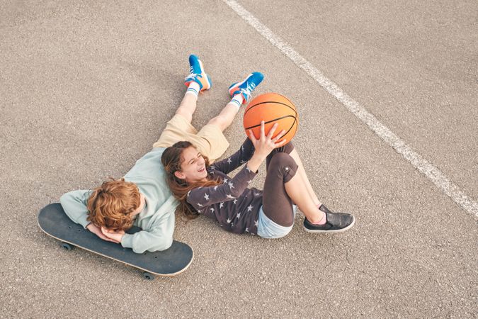 Content teen friends lying on street with skateboard and basketb