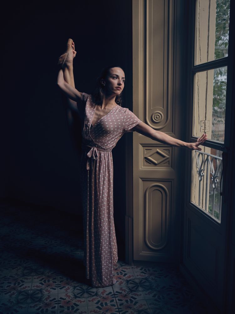 Graceful ballerina performing standing split in dark room