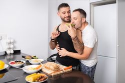 Cute male couple preparing food for lunch and tasing it as they go