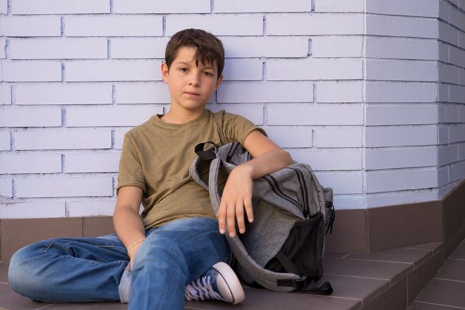 Boy sitting on ground in school corridor with backpack