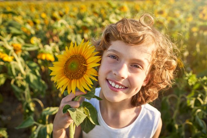 Cheerful boy with sunflower growing in field on sunny day