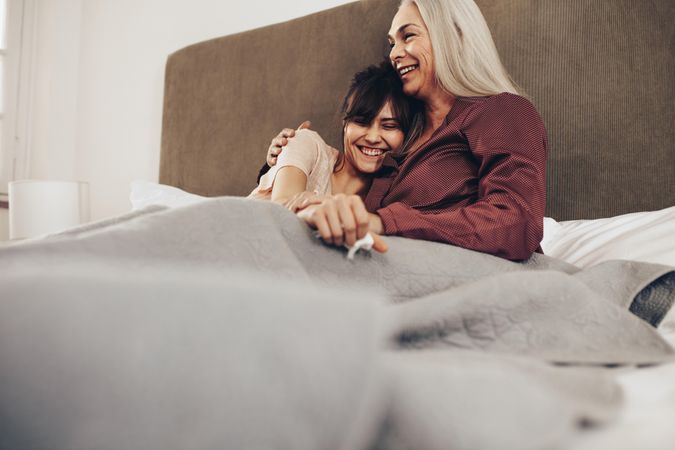 Older woman holding her adult daughter in arm while sitting on bed