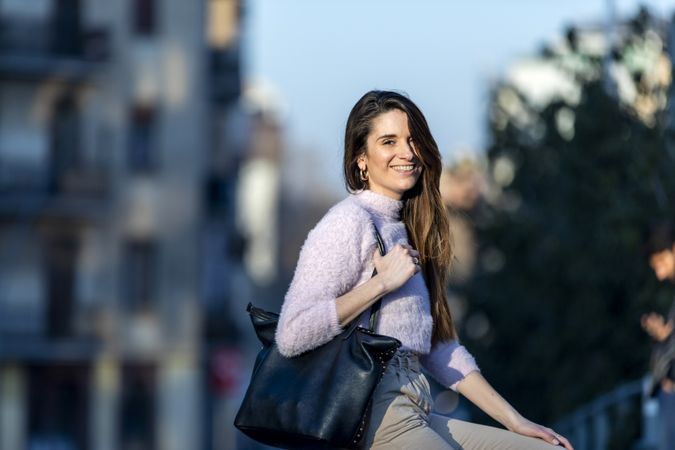 Long haired smiling woman with handbag outside at dusk
