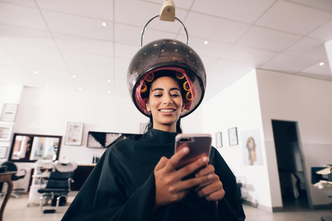Woman at spa with rollers in hair sitting under a hooded dryer