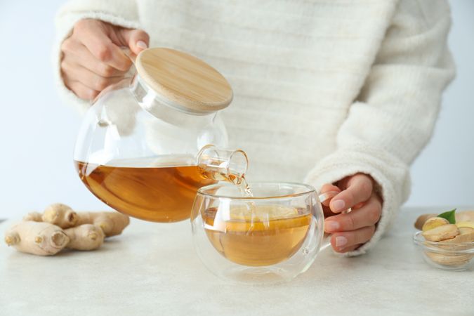 Cup and teapot with tea in female hands, ginger