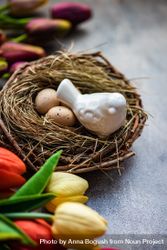 Bird ornament in nest with small eggs surrounded by tulips bxAqMr
