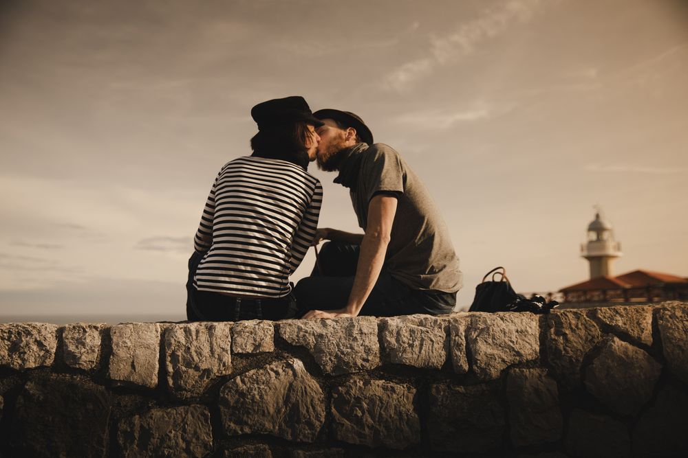 Man kissing woman on stones near lighthouse