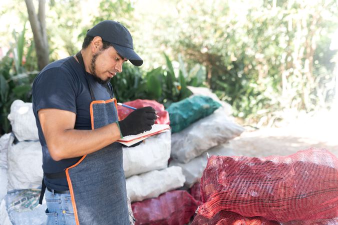 Adult Hispanic Man Recording Weights of Recycled Glass Bottle Sacks for Monitoring