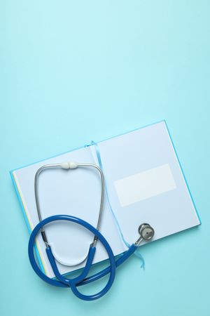 Notepad and stethoscope on blue background, space for text