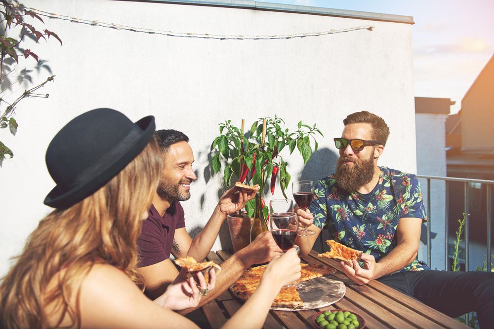 Group of friends on rooftop with red wine and eating pizza