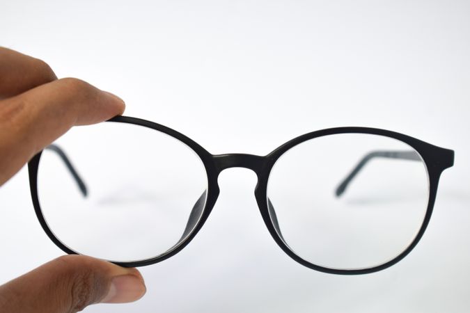 Glasses held by hand on plain background with copy space