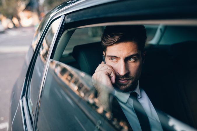 Handsome businessman talking on the mobile phone while sitting on back seat of a car