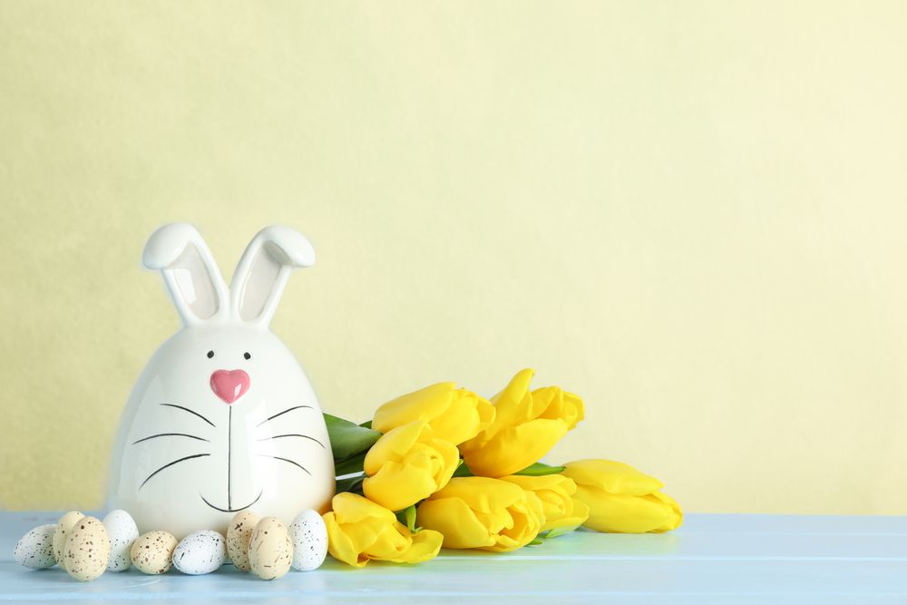 Decorated bunny and Easter eggs on table against color background. Space for text