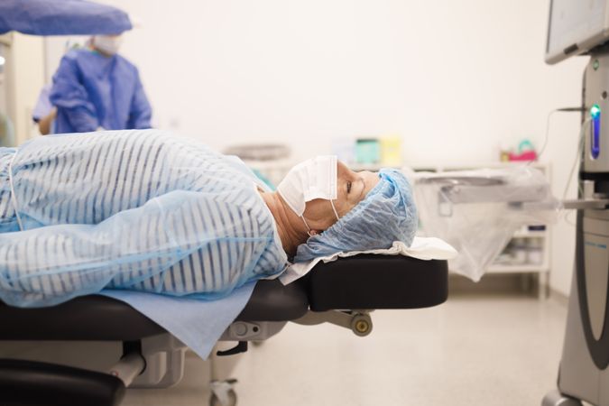 Woman in hair net and facemask lying down pre-surgery