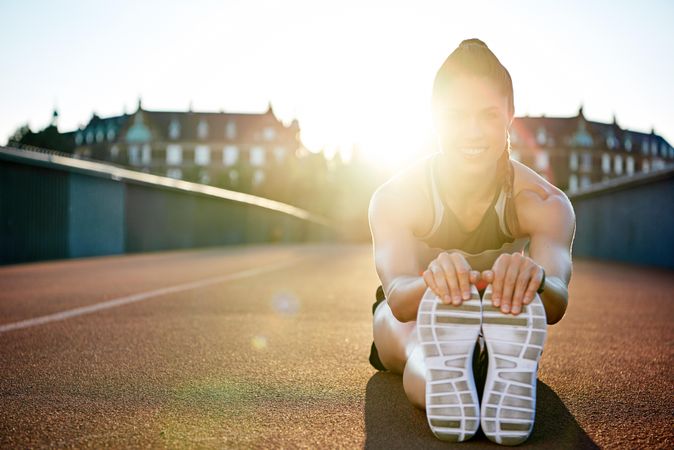 Woman stretching her legs on bridge before workout with sunflare