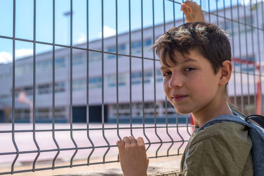 Boy holding fence outside of school yard