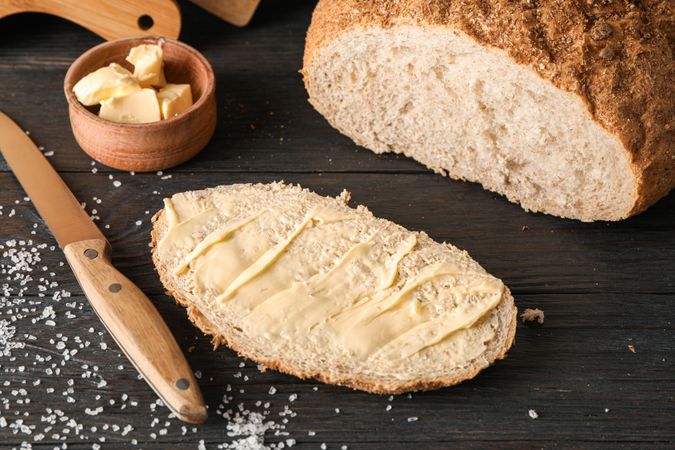 Cutting boards, bread, salt, knife and butter on wooden background, closeup