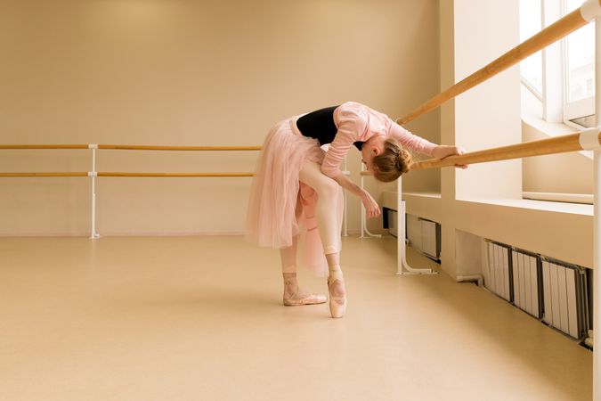 Ballet dancer leaning on barre, stretching in pink tutu