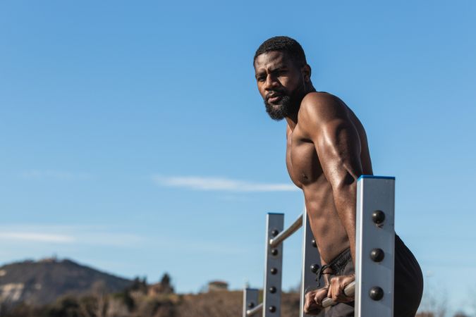Strong Black sportsman working out on bar in town