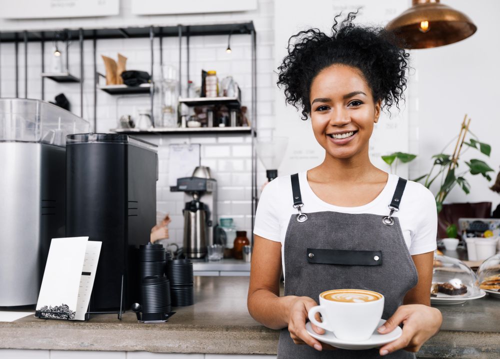 Smiling barista holding a large cappuccino in front of machines
