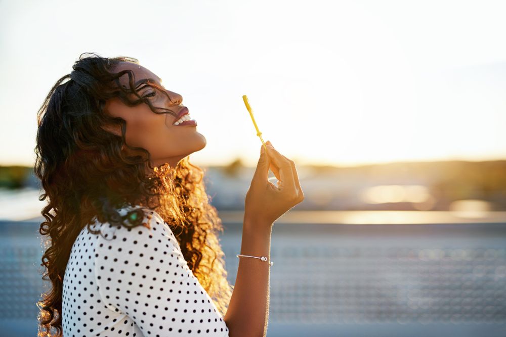 Woman looking up while blowing bubbles on sunny day