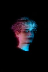 Portrait of blonde young man with UV hair dye against dark background