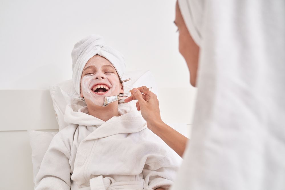 Woman smearing cream mask on face of laughing kid