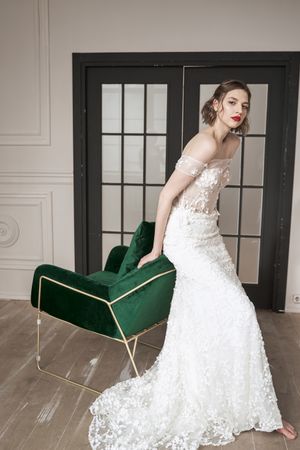 Chic calm woman in white wedding dress leaning on armchair