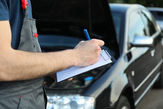 A man in overalls writes to a clipboard. Mechanic. Car inspection