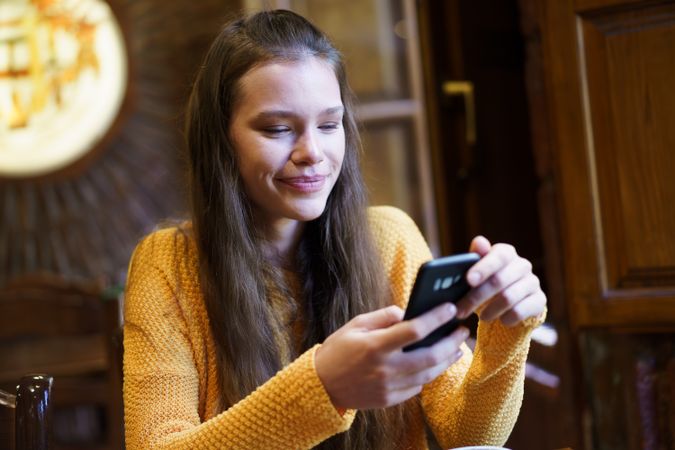 Smiling Young Woman Texting on Smartphone in Cozy Caf