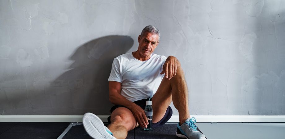 Man resting against wall with water after exercising