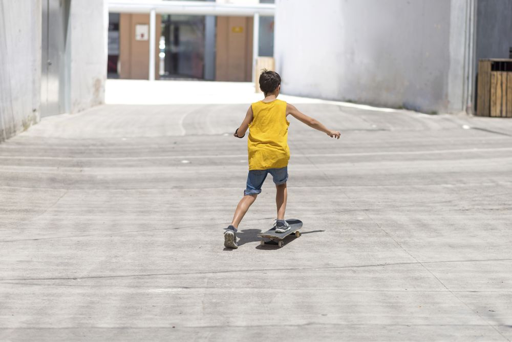 Back of a skater boy riding on the street in the sun