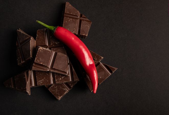 Pieces of yummy chocolate placed with chili pepper on dark background