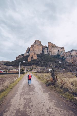 Hiker with backpack walking along rural road to cliff on gloomy day