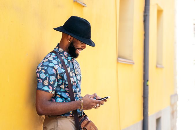 Stylish Black man using smartphone outdoors over yellow background