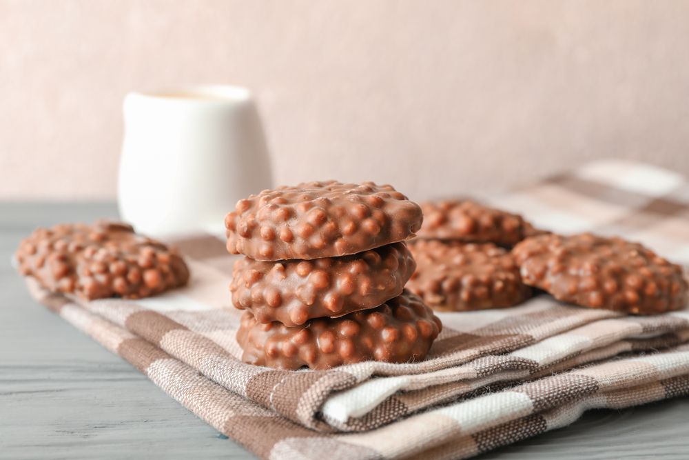 Stack of chocolate cookies on kitchen towel against light background, space for text