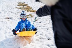 Crop parent pulling sleigh with merry kid