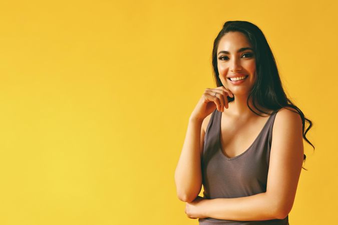 Confident happy Hispanic woman standing and looking at camera in yellow room, copy space