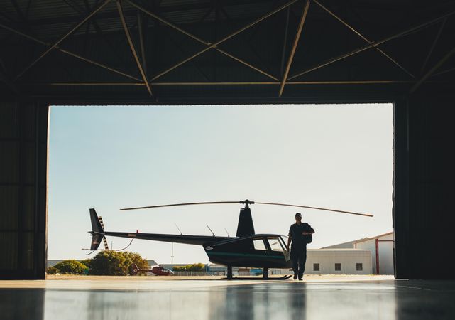 Silhouette of a pilot walking in hangar with a parked helicopter