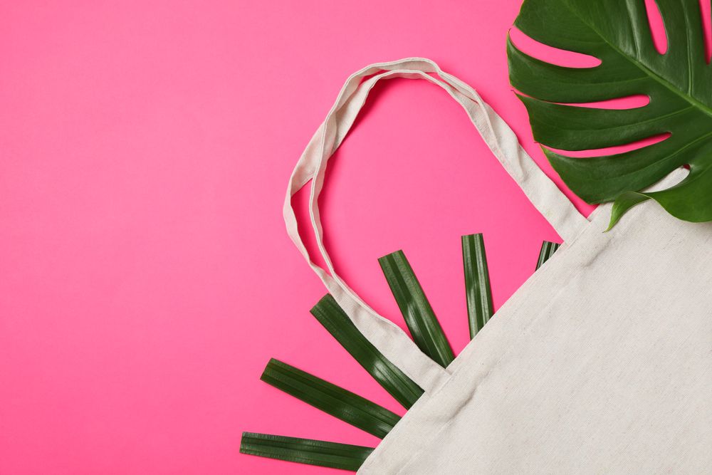 Eco bag and palm leaves on color background, copy space