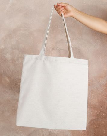 Female hand holding tote bag against brown background, empty space